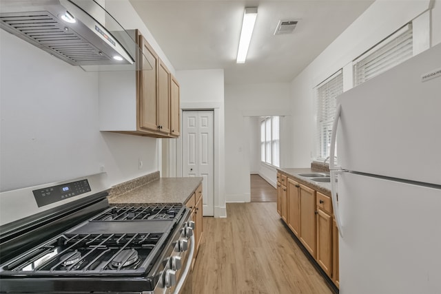 kitchen with wall chimney exhaust hood, stainless steel gas stove, light hardwood / wood-style flooring, and white fridge