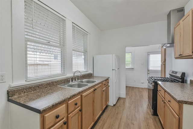 kitchen featuring light hardwood / wood-style floors, white refrigerator, wall chimney exhaust hood, stainless steel gas range, and sink