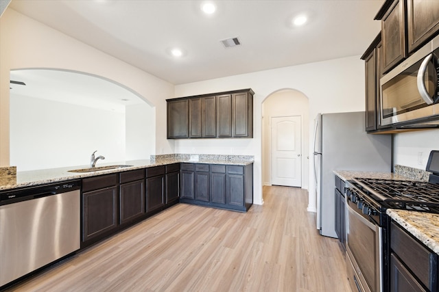 kitchen with dark brown cabinetry, light wood-type flooring, sink, appliances with stainless steel finishes, and light stone countertops