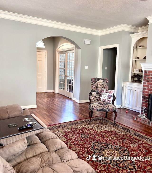 living room with a brick fireplace, built in features, crown molding, dark hardwood / wood-style flooring, and a textured ceiling