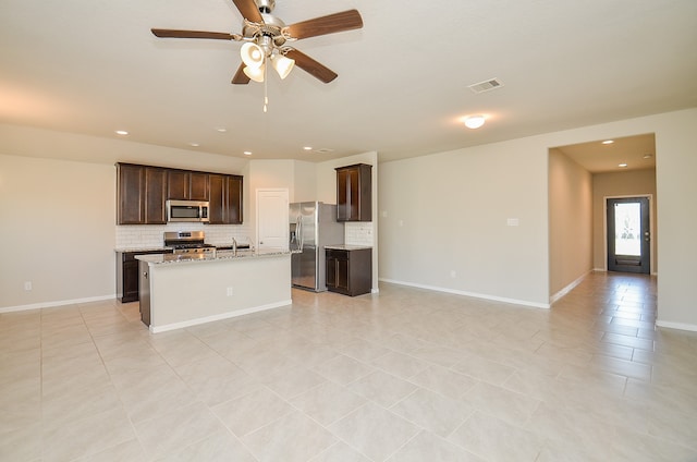 kitchen featuring an island with sink, light tile patterned floors, stainless steel appliances, light stone countertops, and decorative backsplash