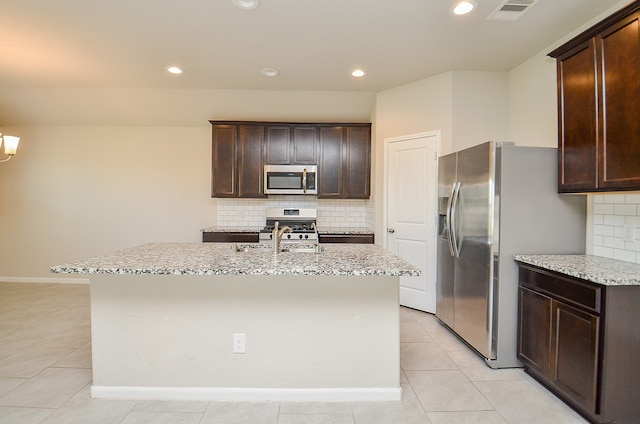 kitchen featuring dark brown cabinets, light stone countertops, a kitchen island with sink, and appliances with stainless steel finishes