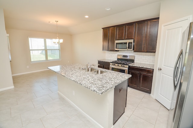 kitchen featuring light stone counters, a kitchen island with sink, sink, appliances with stainless steel finishes, and decorative light fixtures