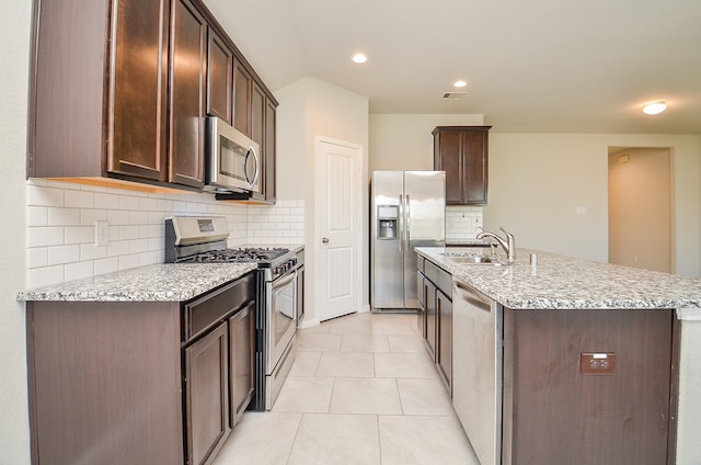 kitchen with decorative backsplash, light tile patterned flooring, a kitchen island with sink, and stainless steel appliances