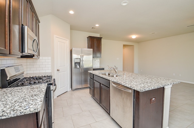 kitchen with light stone counters, backsplash, stainless steel appliances, a kitchen island with sink, and sink