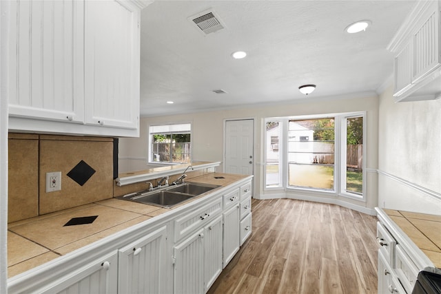 kitchen featuring light wood-type flooring, white cabinets, sink, and tile countertops