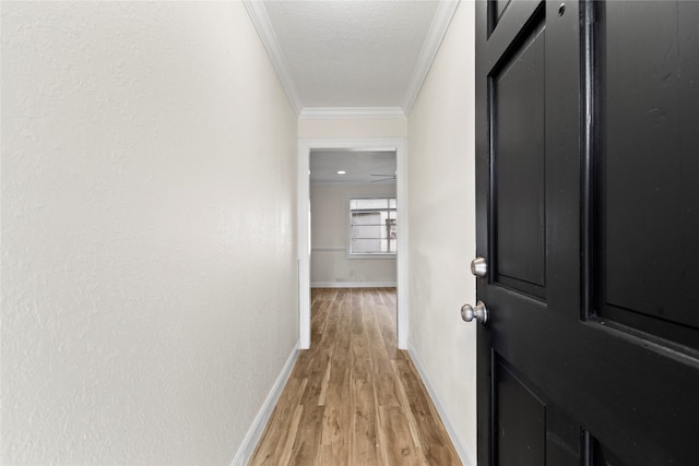 corridor featuring ornamental molding, light wood-type flooring, and a textured ceiling