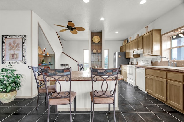 kitchen with a breakfast bar, white dishwasher, ceiling fan, tile counters, and sink