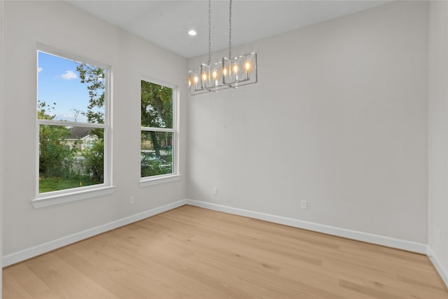 empty room featuring light wood-type flooring, an inviting chandelier, and a healthy amount of sunlight