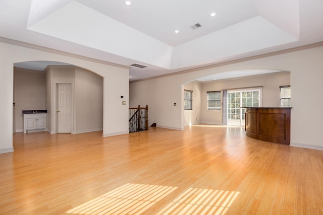 unfurnished living room featuring a tray ceiling, light hardwood / wood-style flooring, and ornamental molding