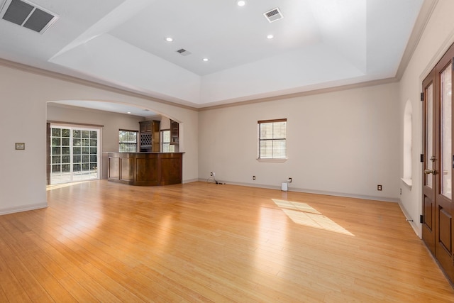 unfurnished living room featuring plenty of natural light, light wood-type flooring, and a tray ceiling