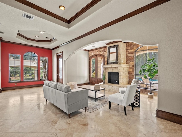 living room featuring crown molding, a stone fireplace, and a raised ceiling