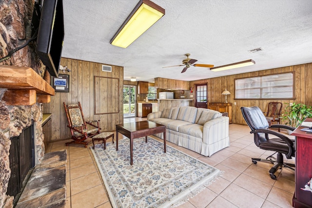 tiled living room featuring wooden walls, ceiling fan, a fireplace, and a textured ceiling