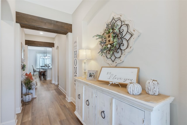 hallway featuring light wood-type flooring, beamed ceiling, and a notable chandelier