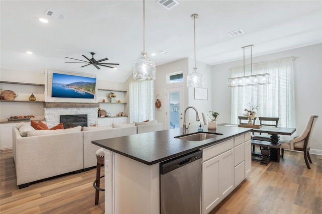 kitchen with a stone fireplace, light hardwood / wood-style flooring, a center island with sink, white cabinetry, and dishwasher