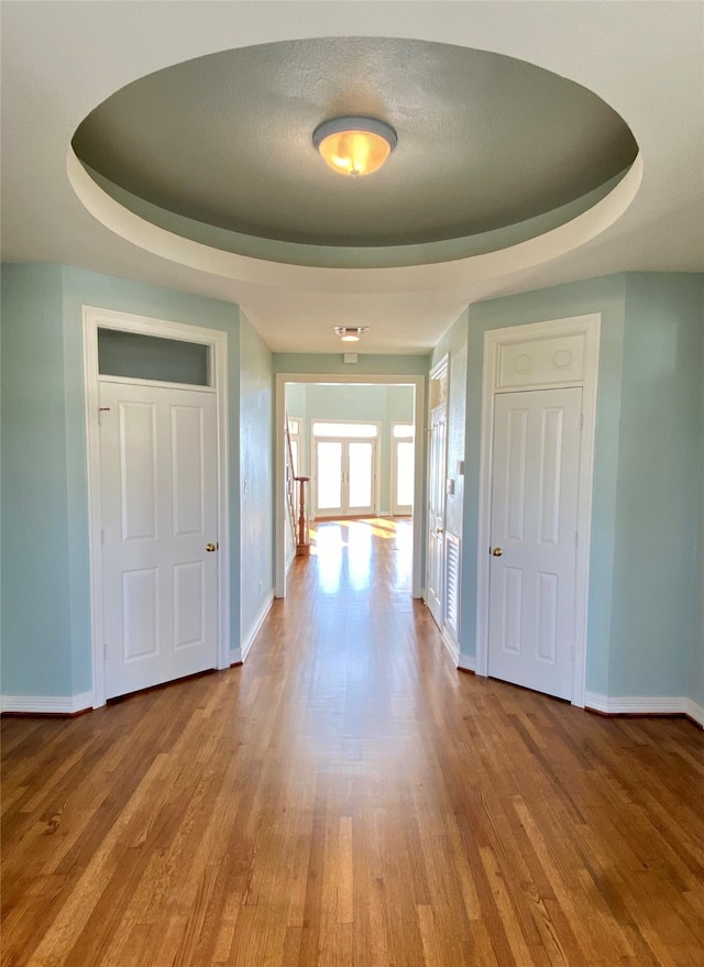 corridor with light wood-type flooring, a raised ceiling, and a textured ceiling