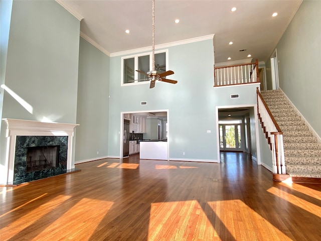 unfurnished living room featuring ceiling fan, dark hardwood / wood-style floors, a high ceiling, a fireplace, and crown molding