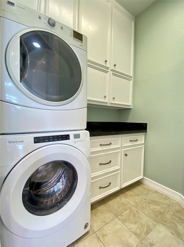 laundry area with cabinets, stacked washer / drying machine, and light tile patterned floors