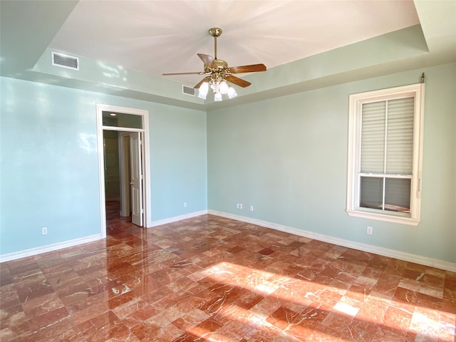 empty room featuring ceiling fan and a raised ceiling