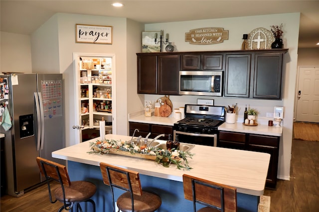 kitchen with a kitchen breakfast bar, dark hardwood / wood-style floors, appliances with stainless steel finishes, and dark brown cabinets