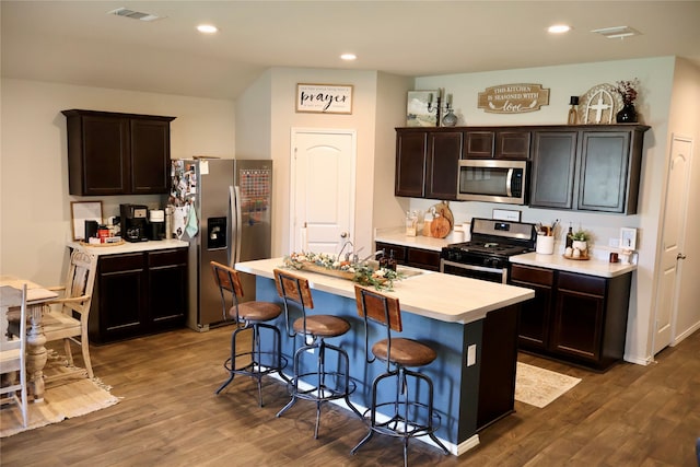 kitchen with dark brown cabinets, an island with sink, appliances with stainless steel finishes, and dark hardwood / wood-style floors