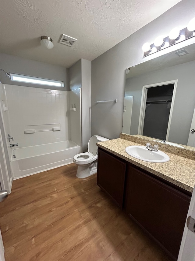 full bathroom featuring vanity, a textured ceiling, hardwood / wood-style flooring, bathing tub / shower combination, and toilet