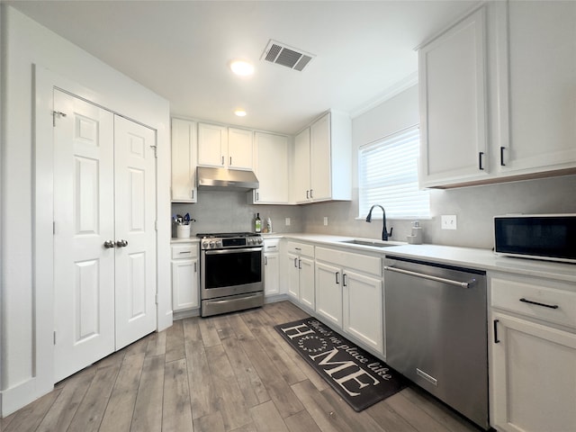 kitchen featuring light wood-type flooring, sink, white cabinetry, appliances with stainless steel finishes, and crown molding