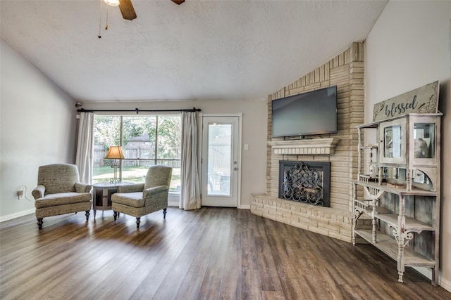 living area featuring vaulted ceiling, a fireplace, a textured ceiling, wood-type flooring, and ceiling fan