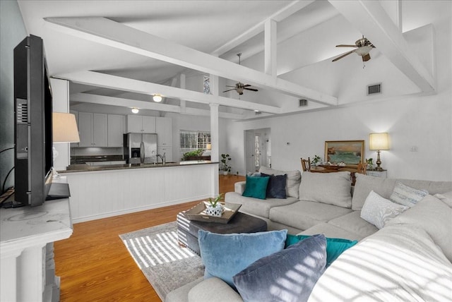 living area featuring ceiling fan, beam ceiling, high vaulted ceiling, light wood-type flooring, and visible vents