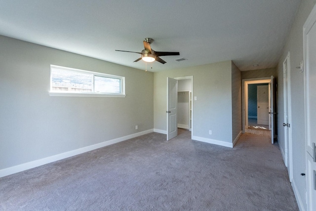 unfurnished bedroom with a walk in closet, visible vents, a ceiling fan, carpet flooring, and baseboards