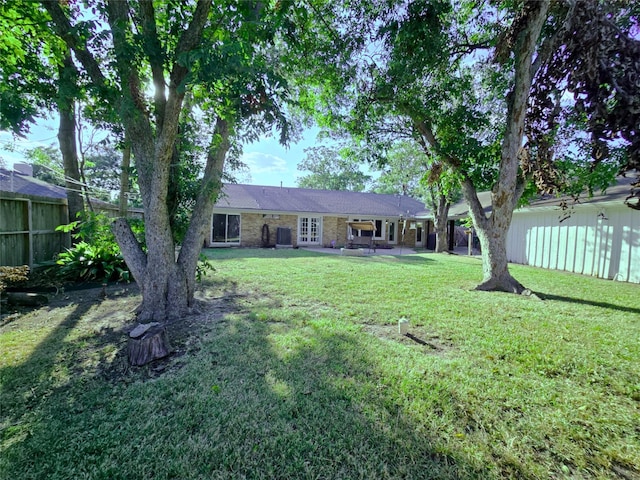 view of front of home with a patio, fence private yard, brick siding, french doors, and a front lawn