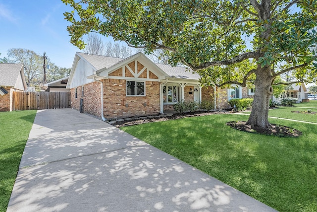 view of front of property featuring a front yard, fence, driveway, roof with shingles, and brick siding