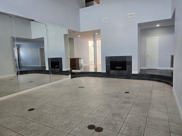 unfurnished living room featuring a high ceiling, a tiled fireplace, and light tile patterned floors