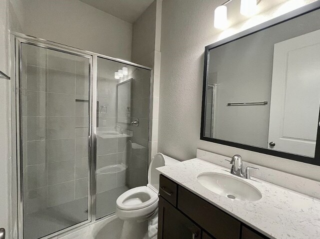 bathroom with a shower with shower door, vanity, and toilet