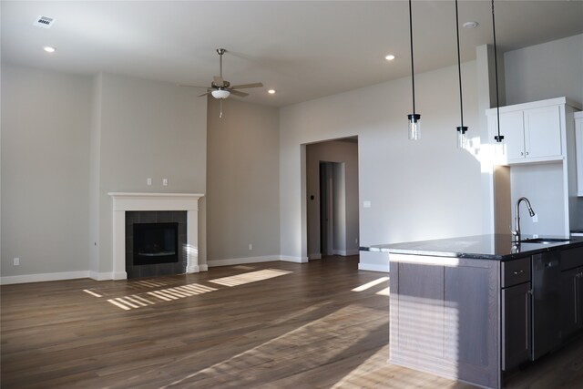 kitchen featuring a tiled fireplace, dark wood-type flooring, sink, hanging light fixtures, and an island with sink