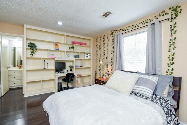 bedroom with built in desk, a textured ceiling, ensuite bath, and dark hardwood / wood-style flooring