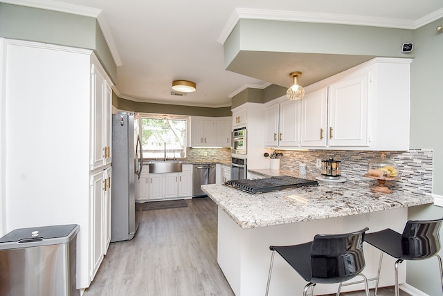 kitchen featuring kitchen peninsula, backsplash, white cabinetry, appliances with stainless steel finishes, and a kitchen breakfast bar