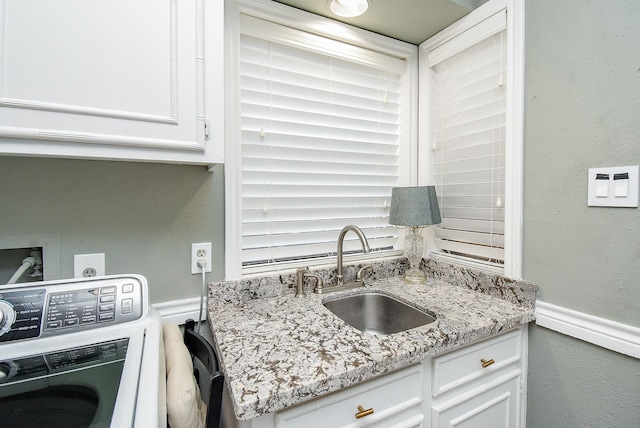 kitchen featuring sink, light stone countertops, white cabinetry, and washer / dryer