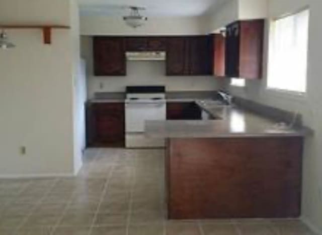 kitchen with white range, kitchen peninsula, light tile patterned floors, and exhaust hood