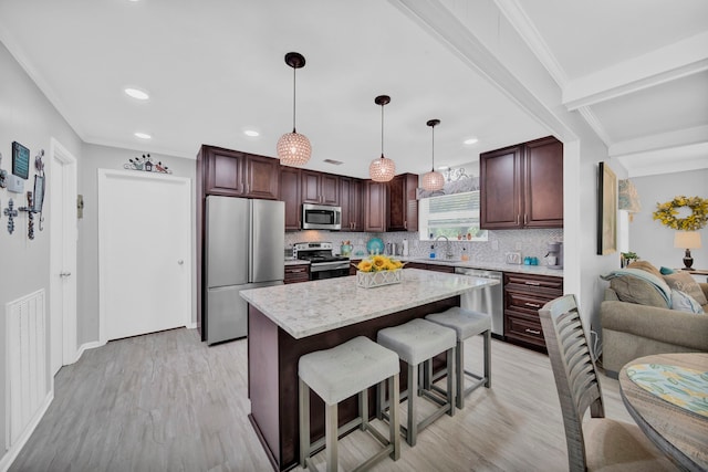 kitchen with appliances with stainless steel finishes, light hardwood / wood-style floors, backsplash, a kitchen island, and decorative light fixtures