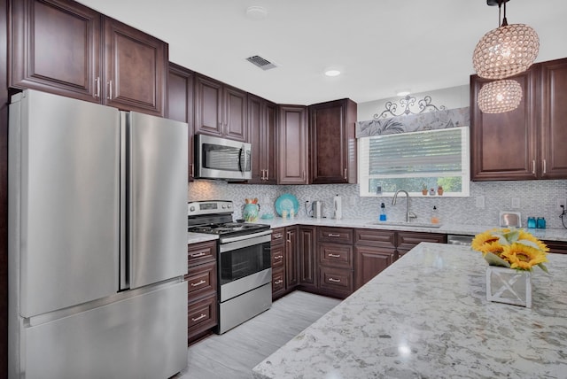 kitchen featuring tasteful backsplash, sink, appliances with stainless steel finishes, decorative light fixtures, and light stone countertops