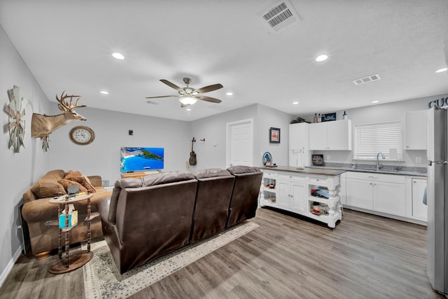 living room featuring ceiling fan, light hardwood / wood-style flooring, and sink