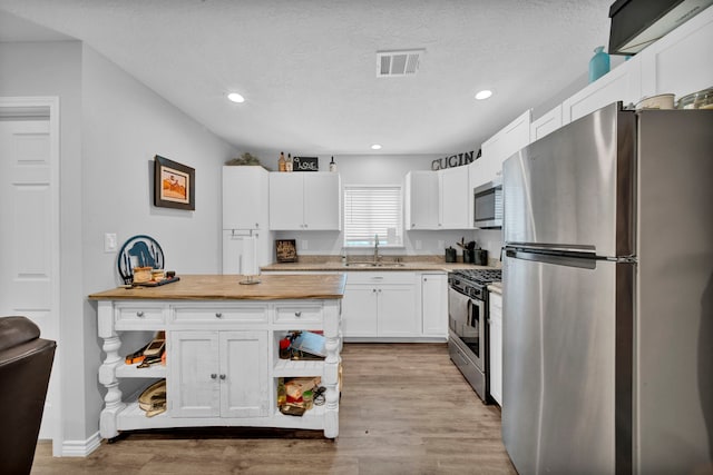 kitchen with white cabinets, a textured ceiling, stainless steel appliances, and light hardwood / wood-style floors