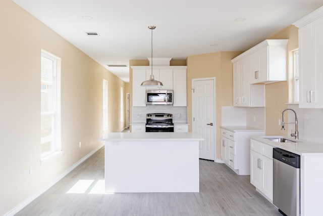 kitchen with appliances with stainless steel finishes, light hardwood / wood-style floors, white cabinetry, and a kitchen island