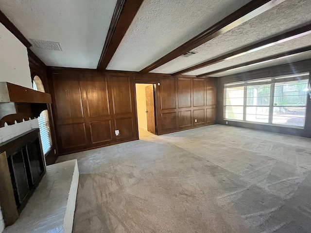 unfurnished living room with beamed ceiling, a textured ceiling, light colored carpet, and wooden walls