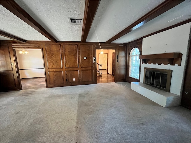 unfurnished living room with light colored carpet, beam ceiling, wooden walls, and a textured ceiling