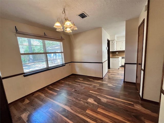 spare room with a notable chandelier, dark wood-type flooring, and a textured ceiling