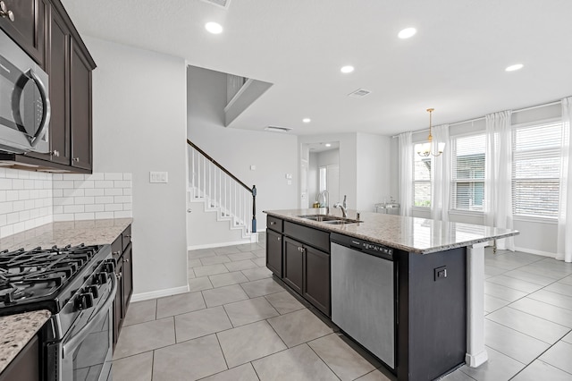 kitchen featuring a kitchen island with sink, sink, backsplash, appliances with stainless steel finishes, and light stone countertops