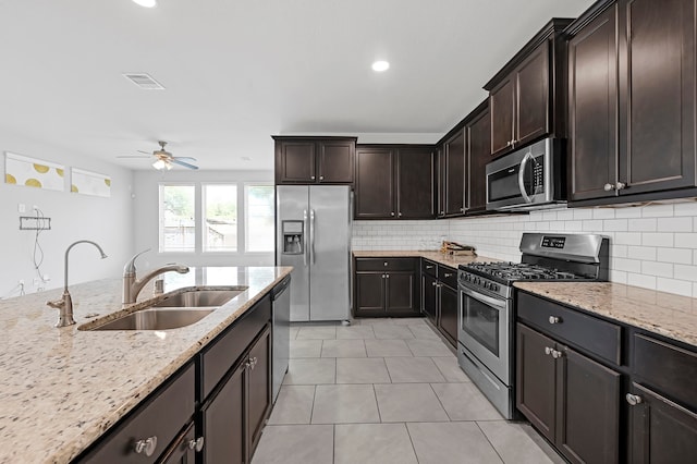 kitchen featuring dark brown cabinetry, light tile patterned floors, sink, appliances with stainless steel finishes, and light stone countertops