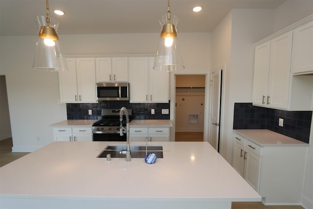 kitchen with pendant lighting, a kitchen island with sink, stainless steel appliances, white cabinets, and decorative backsplash